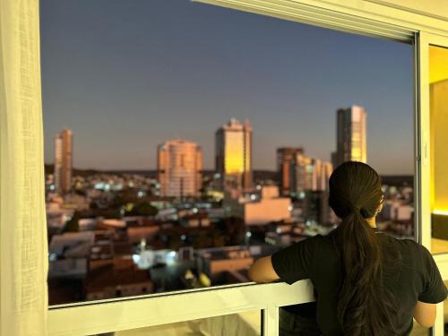 a woman looking out of a window at a city at Apartamentos Exclusivos no Edifício City House in Barreiras