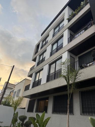 a white apartment building with a palm tree in front of it at Superbe T2 moderne au cœur du Maarif Confort & Style in Casablanca