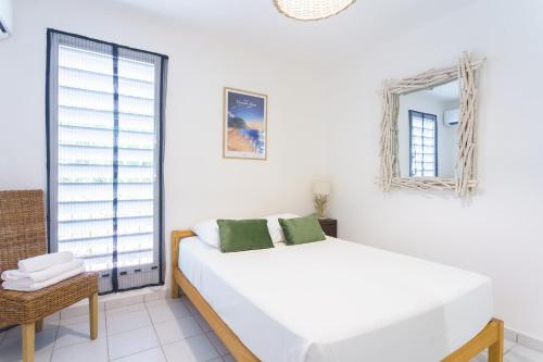 a white bedroom with a bed and a mirror at Bel appartement au calme et cosy à deux pas de la plage in Le Gosier