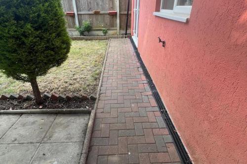 a brick sidewalk next to a red wall with a tree at 4-Bed Barnwell Retreat- Sleeps 9 Garden & Parking in Stevenage