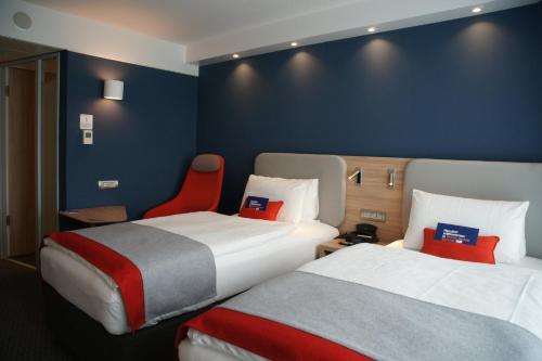 a hotel room with two beds and a red chair at Holiday Inn Express Zürich Airport by IHG in Rümlang