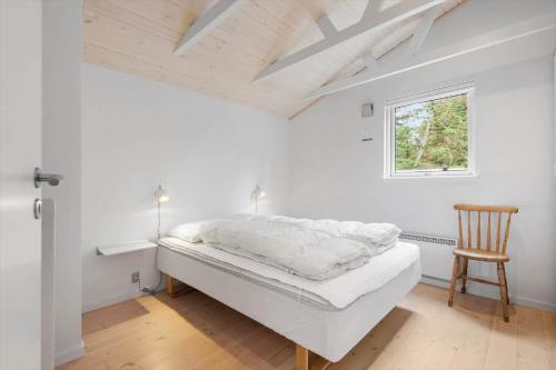 a white bedroom with a bed and a wooden chair at BV325-Blavand-Tvaervaenget-8 in Blåvand