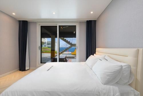 a bedroom with a white bed and a sliding glass door at Gangneung the One and the Classic Pension in Gangneung