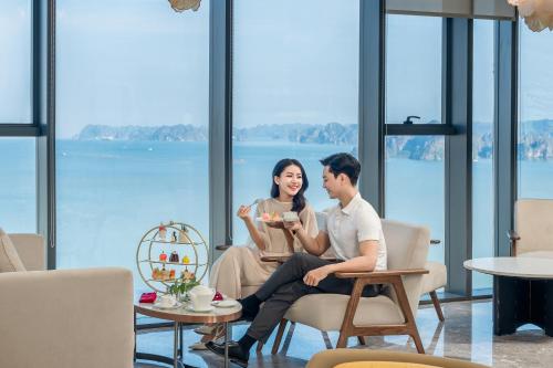 a man and a woman sitting in chairs in a room with windows at A La Carte Ha Long Bay Managed by TASECO in Ha Long