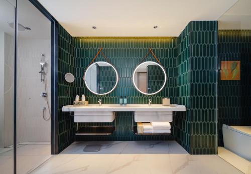 a bathroom with green tiled walls and two mirrors at Novotel Xiamen Downtown in Xiamen