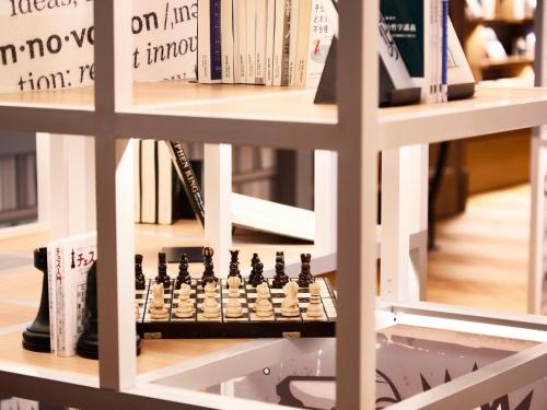 a book shelf filled with books and a chessboard at IN THE LIBRARY hotel and books TOKOROZAWA - Opening in 15th July 2025 in Tokorozawa