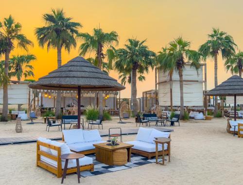 a beach with chairs and tables and palm trees at Marina Hotel in Kuwait
