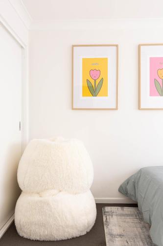 a white chair in a bedroom with two pictures on the wall at Lake Illawarra Family Escape in Lake Illawarra