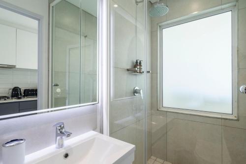Un baño con lavabo y ducha con espejo. en Stylish Studio in One on Albert, en Hout Bay