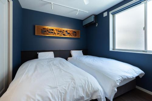 two beds in a room with blue walls and a window at yah homes takasago in Fukuoka