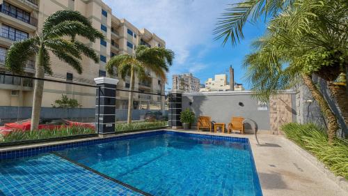 a swimming pool with palm trees and a building at Marmeu Tombo in Guarujá