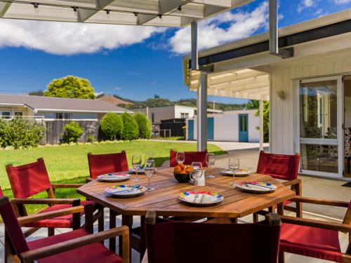 a wooden table with red chairs on a patio at Gone Coastal - Whangamata Holiday House in Whangamata