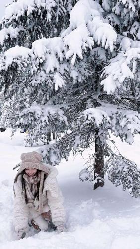 a woman kneeling in the snow in front of a tree at Six-rafter Hall designer hot spring inn in Shangzhi