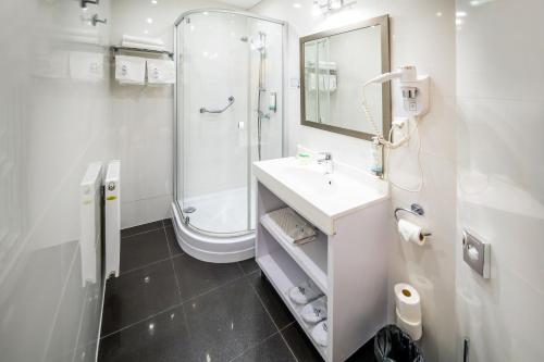 a white bathroom with a sink and a shower at Hotel Jantar Wellness & Spa in Ustka