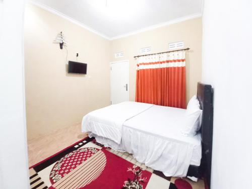 a bedroom with a white bed and a red curtain at Lancar Homestay Syariah near BNS Mitra RedDoorz in Tlekung