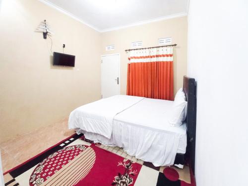 a bedroom with a white bed and a red curtain at Lancar Homestay Syariah near BNS Mitra RedDoorz in Tlekung