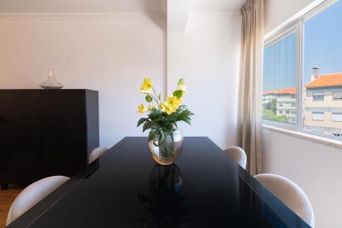 a black table with a vase with yellow flowers on it at Carcavelos Blue Sea II in Carcavelos