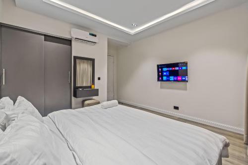 a white bedroom with a bed and a tv at Zuma Nest in Lagos