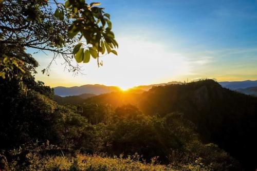 a sun setting over a mountain range with trees at Villa De Sunrise spice garden in Kadugannawa