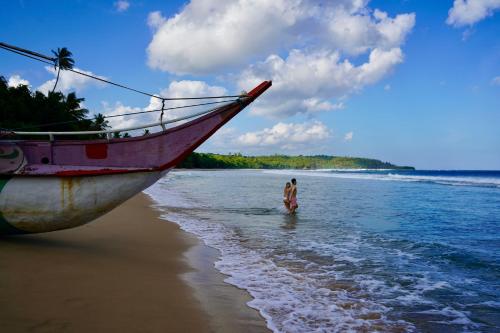 a person standing on the beach next to a boat at The Cabana Hotel Hiriketiya in Dickwella