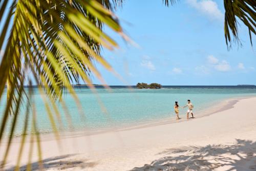 a couple walking on the beach at ROBINSON NOONU - All Inclusive in Manadhoo