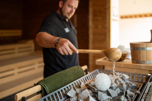 a man cooking food on a grill with a wooden spoon at ADEA Lifestyle Suites Fieberbrunn in Fieberbrunn