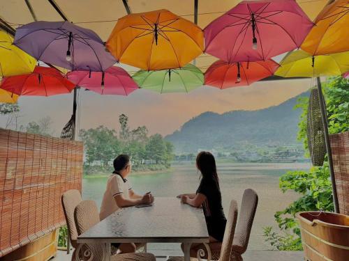 two people sitting at a table with umbrellas at Nhà Ven Hồ Đồng Đò, Minh Trí, Sóc Sơn, Hà Nội in Hanoi