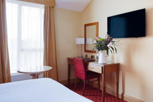 a hotel room with a bed and a desk with a television at Kettles Country House Hotel in Swords