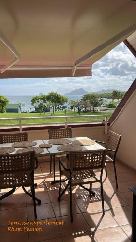 a patio with tables and chairs and a view of the ocean at T3 Rhum Passion vue mer et rocher du Diamant dans célèbre Village de Vacances in Sainte-Luce