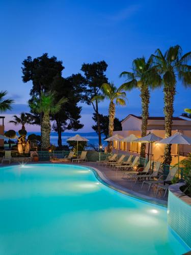 a pool with chairs and palm trees at night at Aegean Melathron Thalasso Spa Hotel in Kallithea Halkidikis