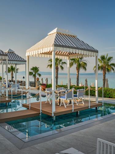 a resort pool with chairs and a gazebo at Aegean Melathron Thalasso Spa Hotel in Kallithea Halkidikis