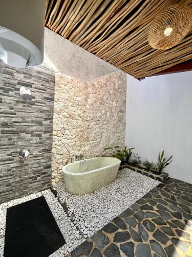 a bath tub in a bathroom with a stone wall at Villa Suaka by Sackstone in Watukarung