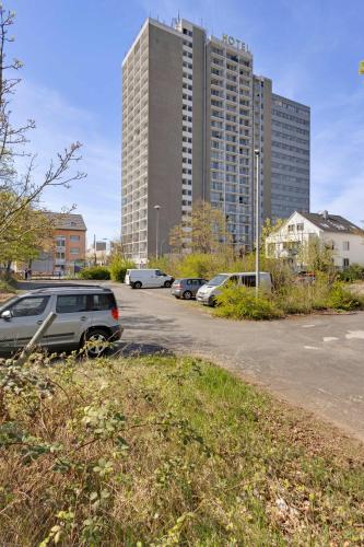 a parking lot with cars parked in front of a tall building at Hotel Montago- Dein großes Zimmer mit hervorragender Infrastruktur in Neu Isenburg