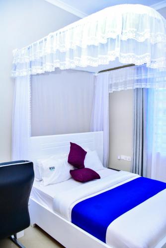 a white bed with purple pillows and a window at KER HOTEL Dodoma in Dodoma