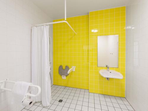 a yellow tiled bathroom with a sink and a mirror at B&B Hotel Mülheim an der Ruhr in Mülheim an der Ruhr