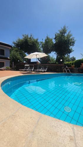 a blue tile swimming pool with an umbrella and chairs at Villa MELANY Casa Vacanza in Piedimonte Etneo