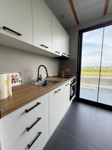 a kitchen with white cabinets and a large window at Villa REJA Hamallaj in Draçi