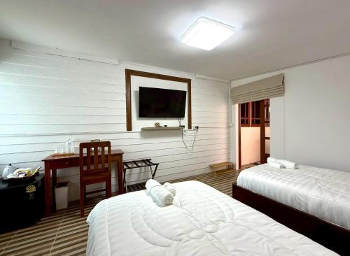 Una habitación de hotel con dos camas, un escritorio y un televisor. en Baan inta hostel - บ้านอินตาโฮสเทล, en Phra Nakhon Si Ayutthaya