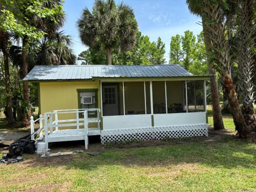 a small yellow cottage with a porch and palm trees at Harmons Landing in Hawthorne