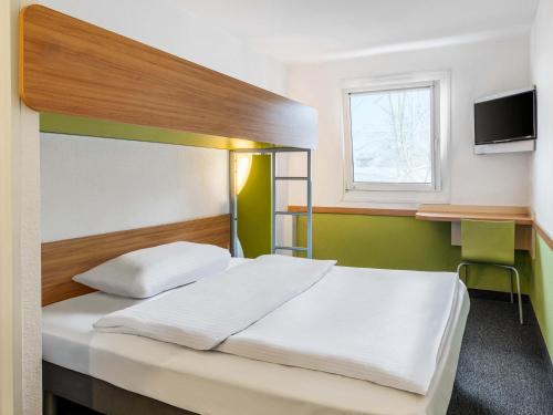 a bedroom with a bed and a desk with a television at B&B HOTEL Aachen-Nord in Aachen