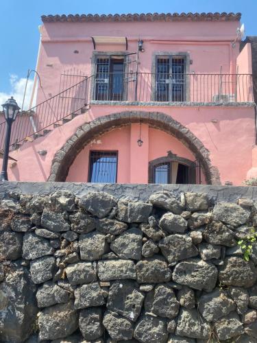 a pink building with a stone wall in front at Le Decime in Mascali