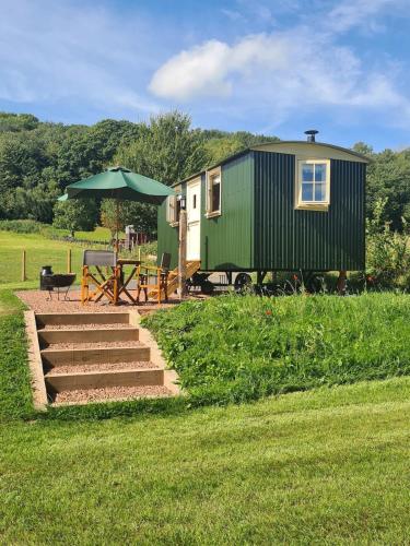a green and white house with a table and an umbrella at Shepherd's Hut in heart of the Brecon Beacons in Bwlch