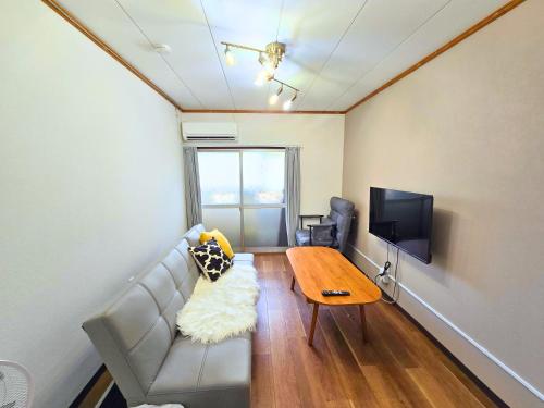 een woonkamer met een bank, een tafel en een tv bij Osaka Riverside Inn in Neyagawa