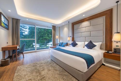 ein Hotelzimmer mit einem großen Bett und einem Schreibtisch und einem Schreibtisch in der Unterkunft Snow Valley Heights - An Elegant Air Conditioned Escape by Snow Valley Resorts in Manali