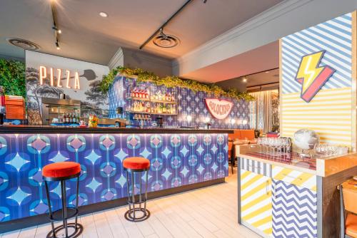 a restaurant with a colorful bar with red stools at Leonardo Hotel Milan City Center in Milan