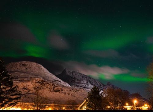 an aurora in the sky over a snow covered mountain at KB Storhaugen House - Sørvågen in Moskenes