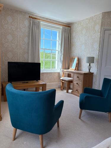 a living room with two blue chairs and a television at Lower Bryanston Farm in Blandford Forum