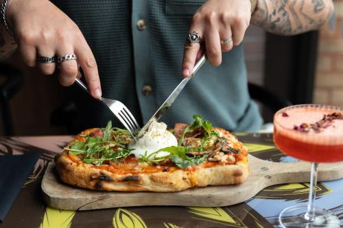 a person cutting into a pizza with two forks and knives at NYX Hotel Dublin Portobello in Dublin