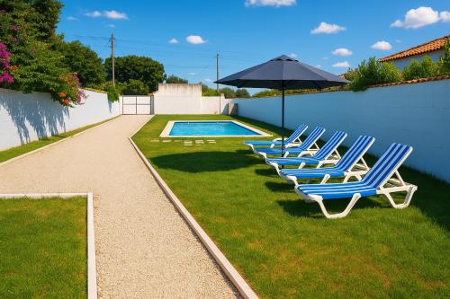 Una fila de sillas de jardín y una sombrilla junto a una piscina. en Casa natural 1, en Chiclana de la Frontera
