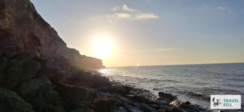 a sun setting over the ocean next to a rocky beach at Seagull Cottage in Hunstanton